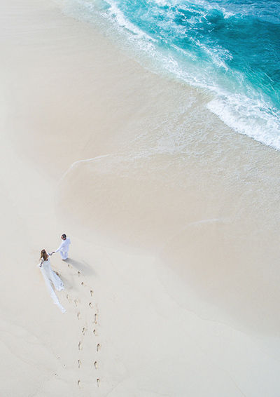 Ein Pärchen macht einen romantischen Spaziergang an weißem Luxus-Sandstrand am türkis-blauen Meer